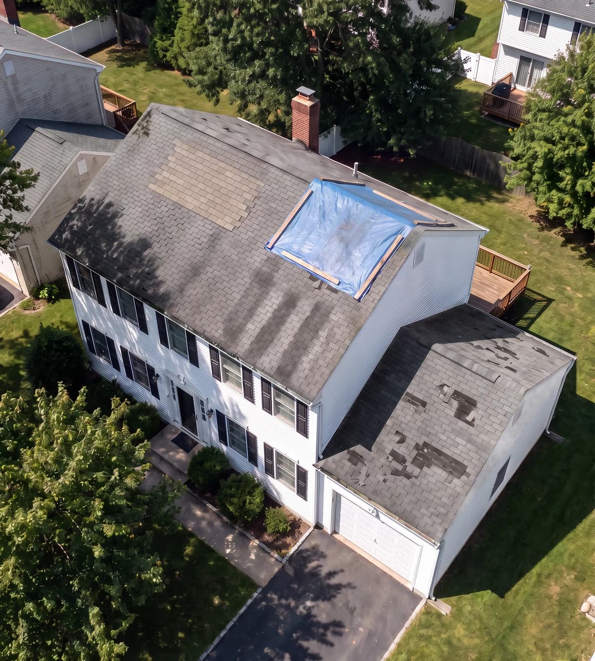 Aerial view of a home whose roof has a tarp, a patch, streaks and missing shingles