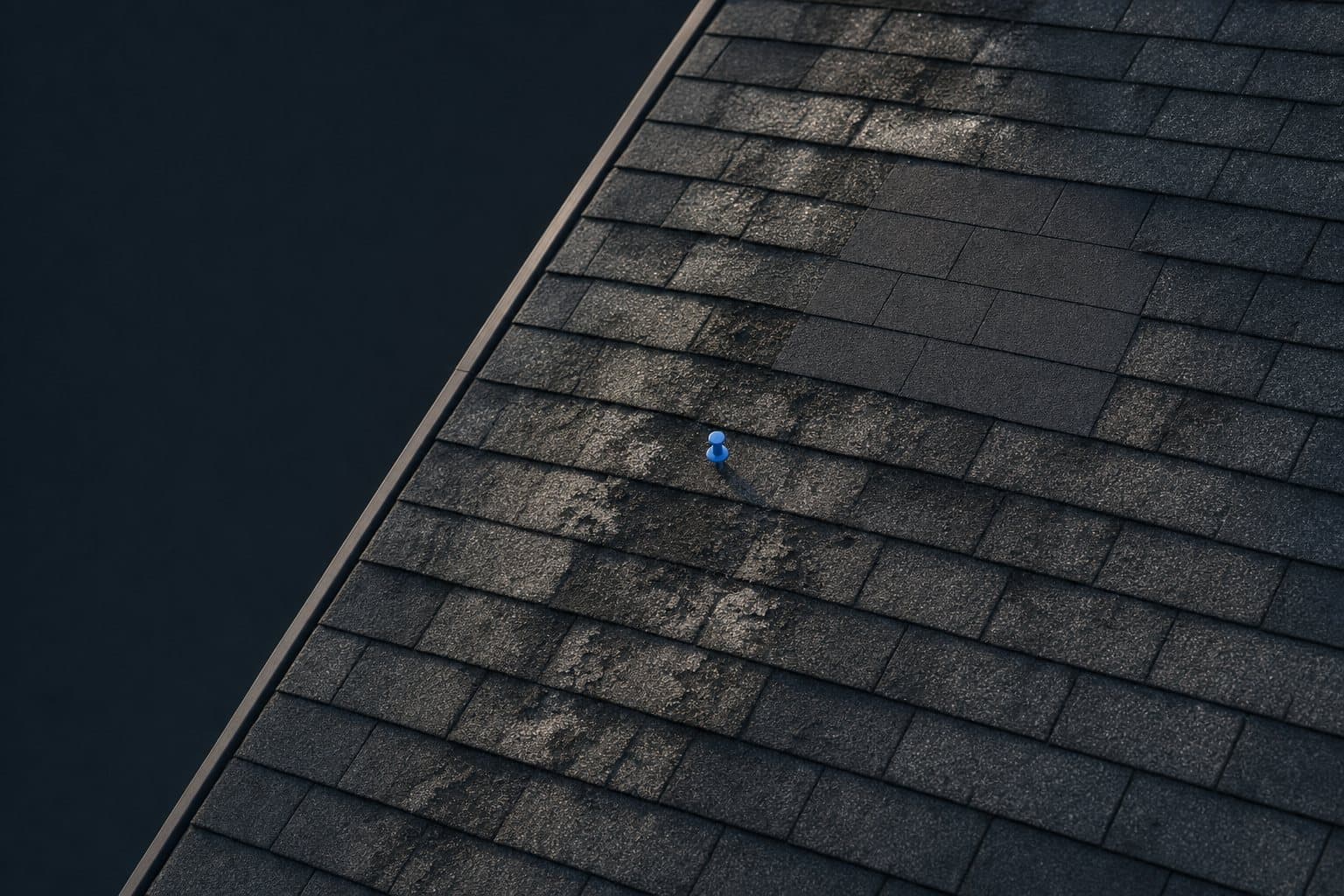 An aged asphalt-shingle roof from above, granule loss and one patched section